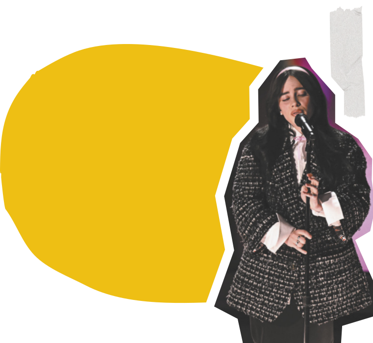 Fotografia de Billie Eilish. Ela é uma mulher jovem, branca, de cabelos longos, lisos e escuros, usa um casaco longo e está cantando em um microfone.