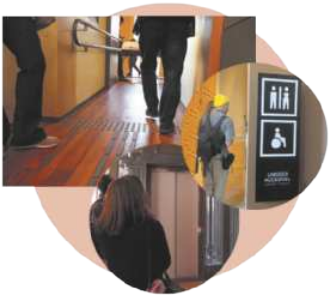 Imagem de uma pessoa caminhando sobre um chão com elementos em alto-relevo. Em destaque, há uma placa com o símbolo de uma pessoa em cadeira de rodas e pessoas aguardando em frente a um elevador.