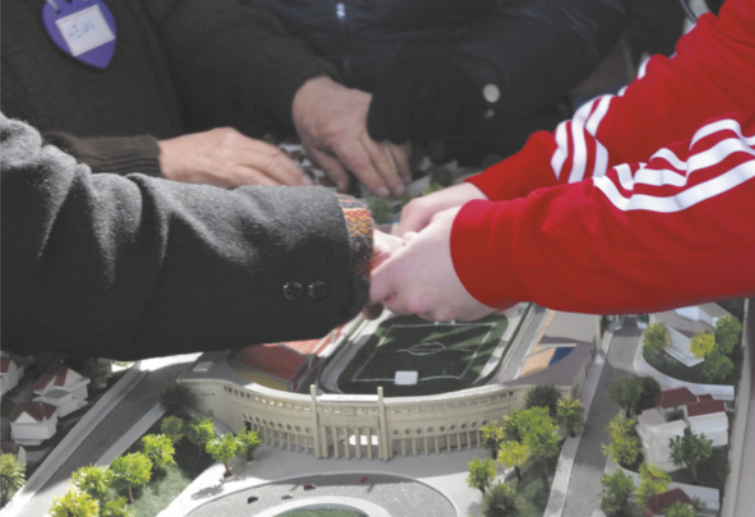 Fotografia de jovens tateando uma maquete representando um estádio de futebol.
