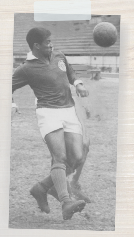 Fotografia em preto e branco de um jogador de futebol em campo, correndo em direção a uma bola que está no ar, em frente ao seu corpo.