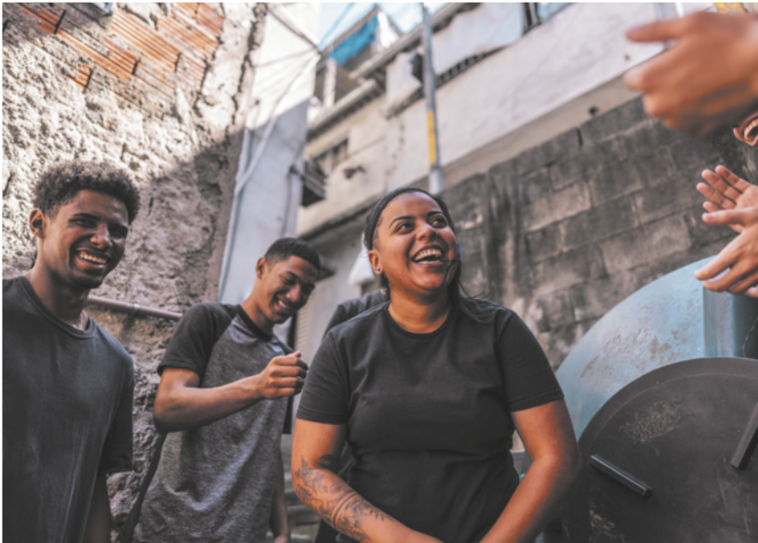 Fotografia de três jovens negros rindo e conversando em uma rua em frente a um muro de concreto.