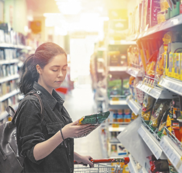 Fotografia de uma mulher em um supermercado segurando um produto nas mãos e lendo o rótulo atentamente.