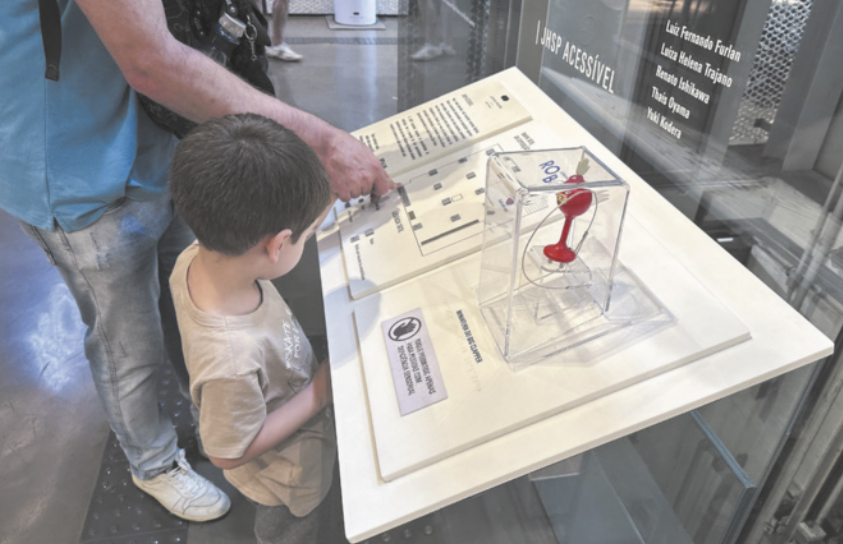 Fotografia de uma criança em um museu tateando um tipo de mapa com a ajuda de um adulto.