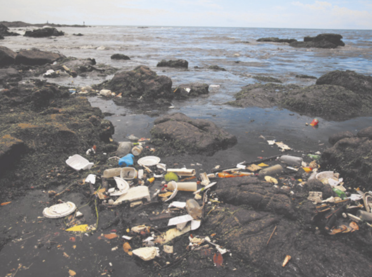Fotografia de um monte de lixo acumulado nas pedras de uma praia.
