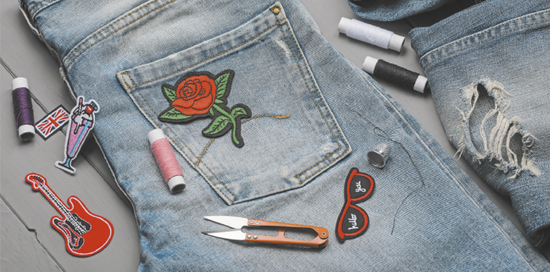 Fotografia de uma calça jeans dobrada com o bolso à mostra. No bolso, há a imagem de uma rosa vermelha costurada e linhas de costura ao redor.