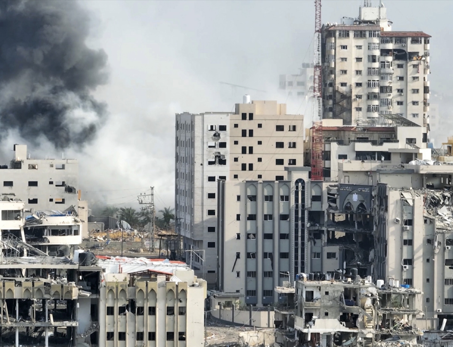 Fotografia de uma cidade com edifícios em ruínas e fumaça de explosões ao fundo.