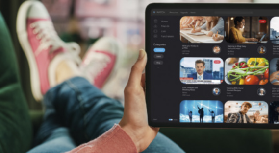 Fotografia de uma pessoa deitada, utilizando um tablet para acessar uma plataforma de streaming com diversas opções de vídeos.