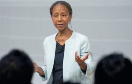 Fotografia de Marian Croak gesticulando enquanto fala para uma plateia. Ela é uma mulher negra, com o cabelo preso.