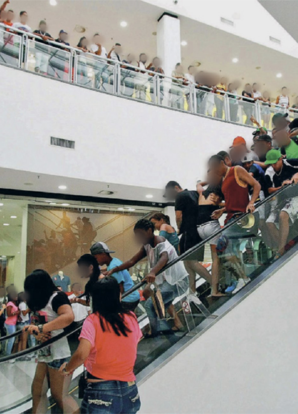 Fotografia do interior de um shopping center com grande fluxo de adolescentes. Em destaque, uma escada rolante repleta de pessoas em movimento. No andar superior, também há um grande grupo de adolescentes reunidos ao longo do guarda-corpo, observando a movimentação no ambiente.