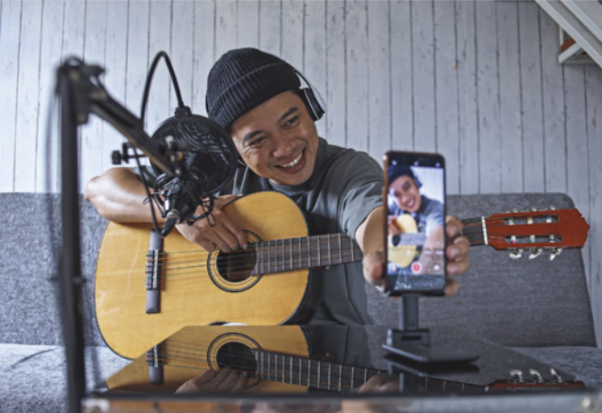Foto de jovem fazendo um vídeo. Ele está tocando violão.