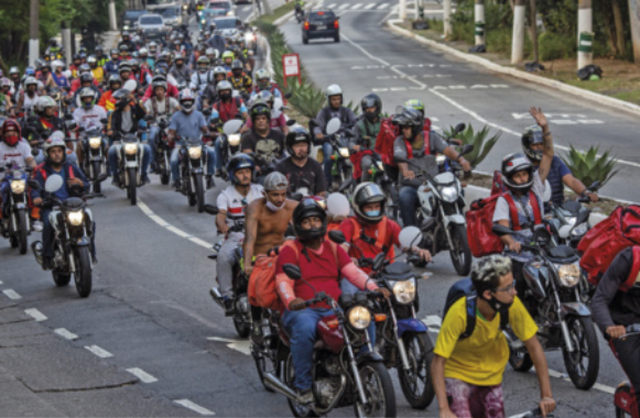 Foto de pessoas protestando. Elas andam juntas de moto.