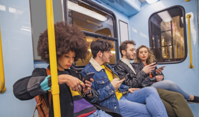 Foto de jovens em um metrô. Eles estão sentados e usam o celular.