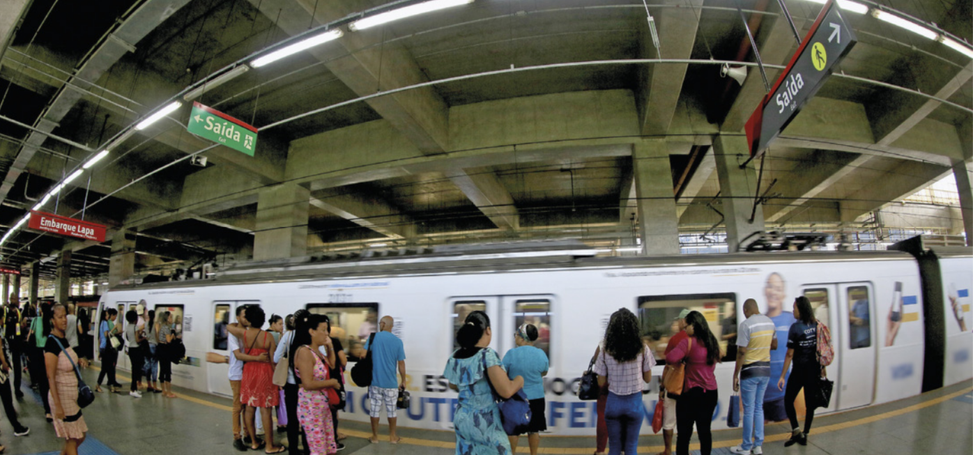 Foto de pessoas na estação de metrô. Há placas sinalizando as saídas e as áreas de embarque.